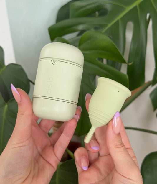 Hands holding green period cup and cleaning case