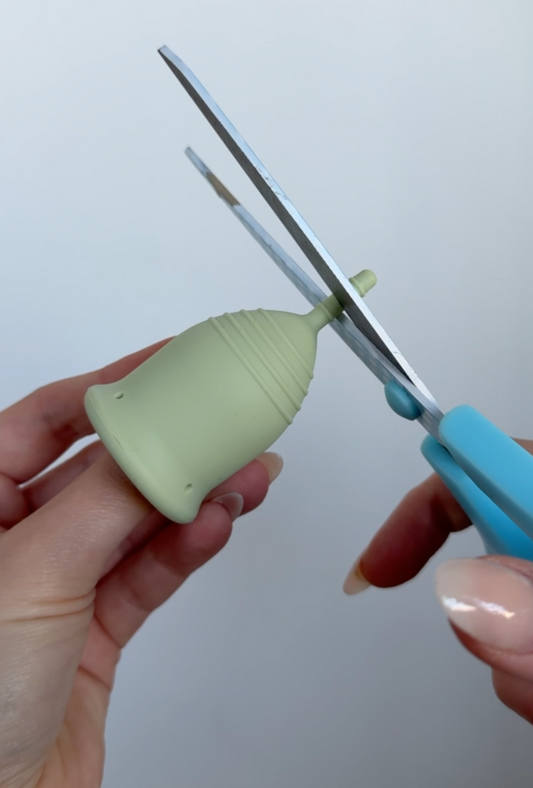Someone using blue scissors to trim a green period cup stem.