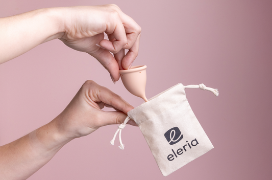 Pink menstrual cup being placed into a cotton drawstring bag