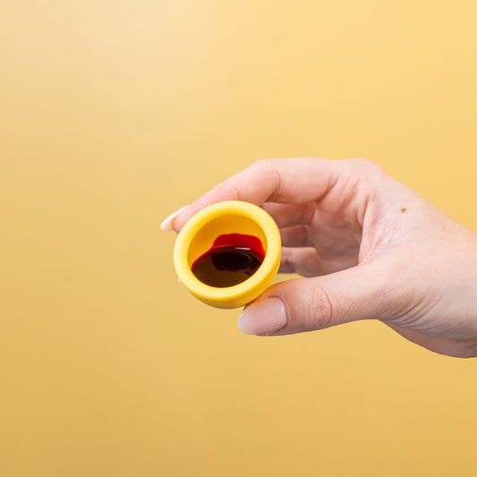 Hand holding a yellow period cup filled with blood against a yellow background.