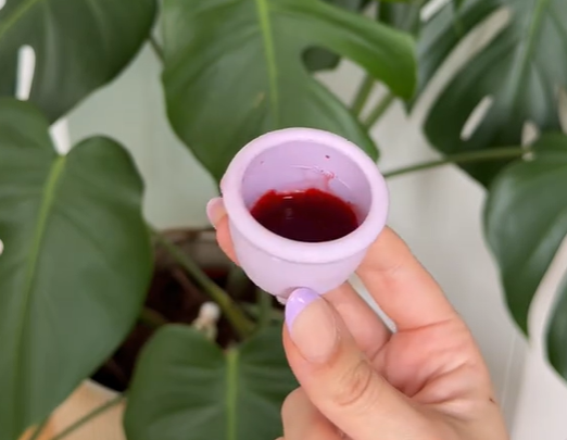 Purple menstrual cup filled with pretend menstrual blood. 