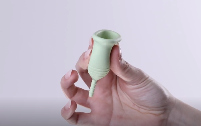 Hand holding green menstrual cup. 